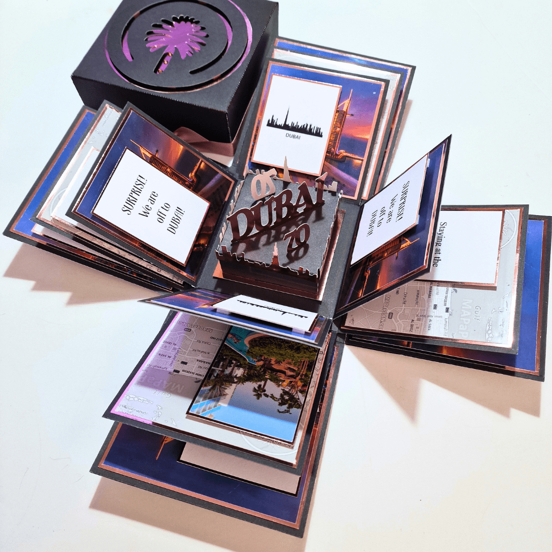 The image shows an elaborate pop-up card themed around Dubai. The card is open, revealing multiple layers and sections with various images and text. The centerpiece features a 3D cutout that says "DUBAI" with a skyline silhouette. Smaller cards and flaps surround it, with phrases like "SURPRISE! We are going to DUBAI" and "Sightseeing at the Burj Khalifa." It's a visually striking and detailed creation.