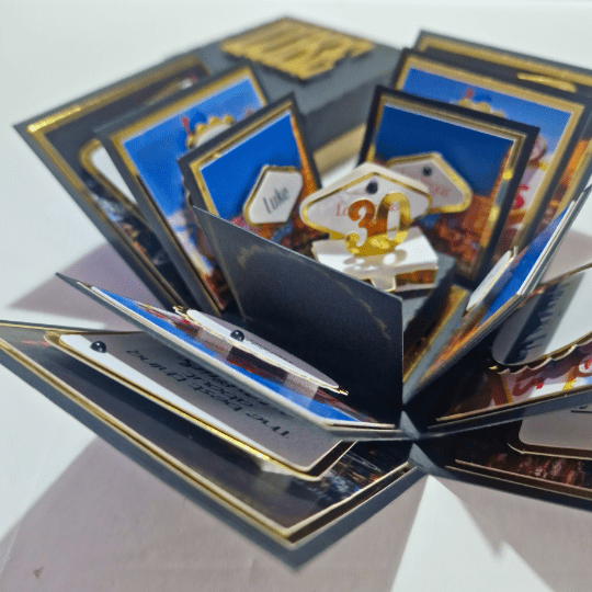 The image shows a pop-up card or an explosion box card that is open, revealing multiple layers and sections with various decorations. The card appears to be intricately designed with multiple flaps and compartments, each containing different elements such as pictures, text, and embellishments. The central part of the card features a "30" in gold, suggesting it might be a birthday or anniversary card. The card is colorful and detailed, making it visually appealing and interesting as a creative and personalized gift.