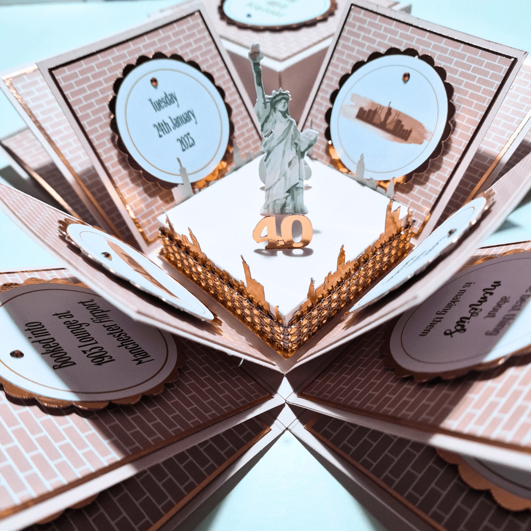 The image shows an intricately designed pop-up card featuring the Statue of Liberty at the center with the number "40" in front of it. The card has multiple panels with text and images, including a date "Tuesday 24th January 2023" and a location "9023 Lounge at Manchester Airport." The panels are decorated with a brick pattern and scalloped edges, and the card appears to be a special invitation or announcement, possibly for a 40th birthday celebration or anniversary. The design is detailed and visually appealing, making it interesting and relevant for special occasions.