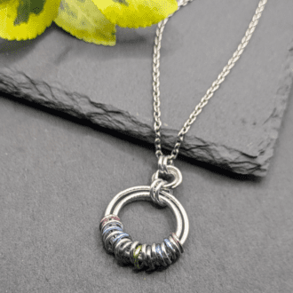 A chainmaille pendant made from aluminium rings. Two large silver coloured rings with smaller pastel coloured rings linking the two larger rings.