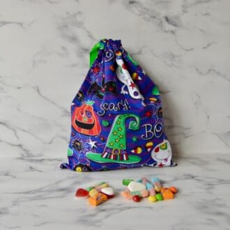 Purple Halloween trick or treat bag with ghosts, witches hats, pumpkins, bats and the words scary and boo written on. The bag has a green ribbon drawstring closure