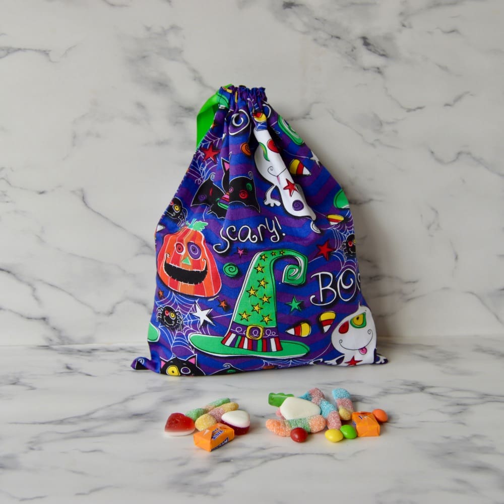 Purple Halloween trick or treat bag with ghosts, witches hats, pumpkins, bats and the words scary and boo written on. The bag has a green ribbon drawstring closure