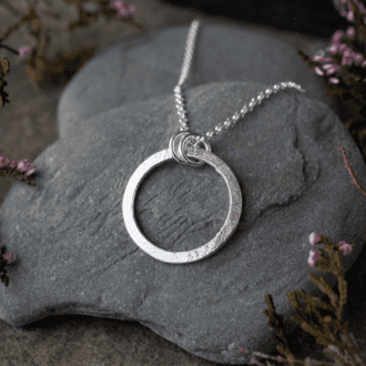 textured silver circle pendant resting on slate pebble