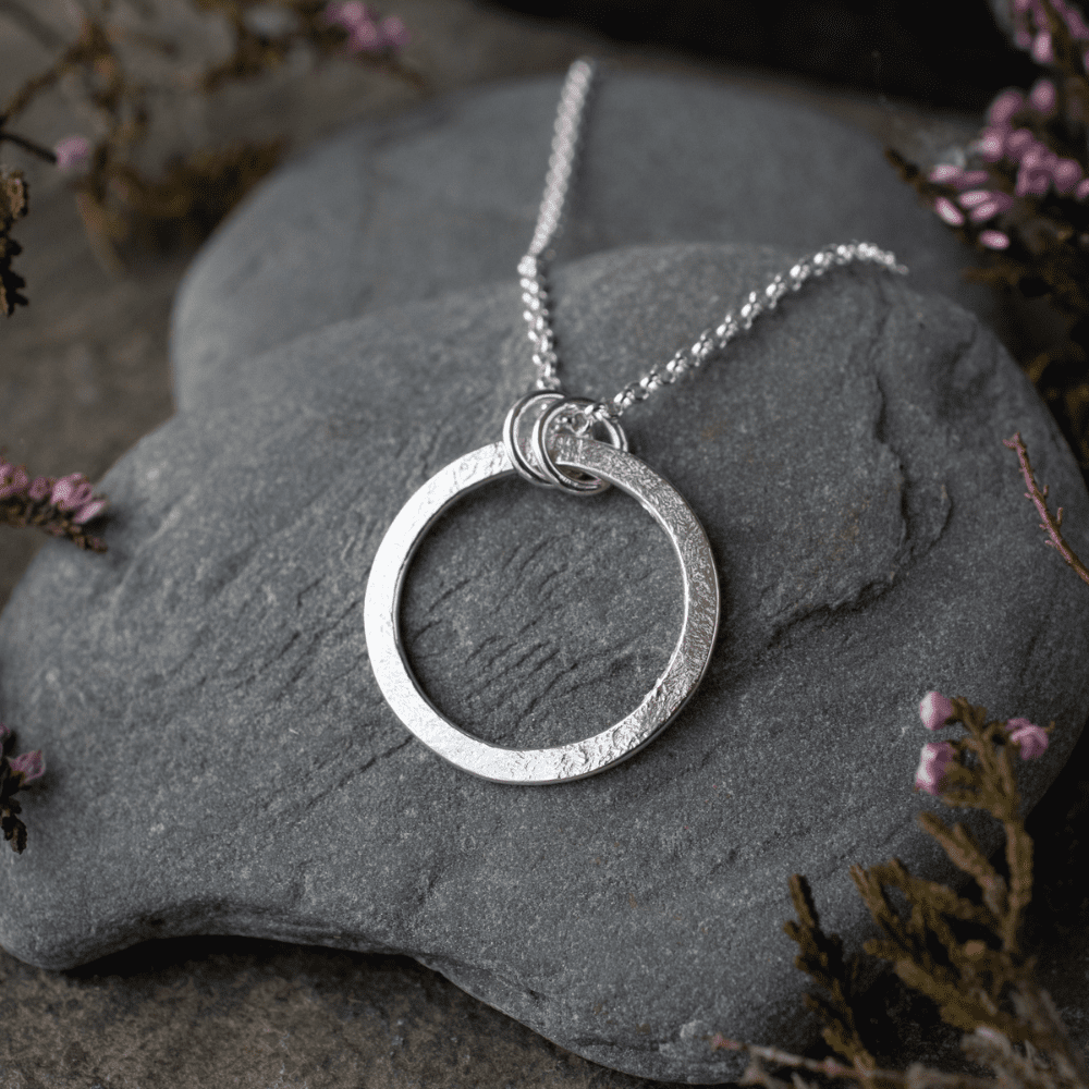 textured silver circle pendant resting on slate pebble