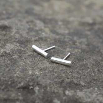 tiny silver line stud earrings resting on a stone