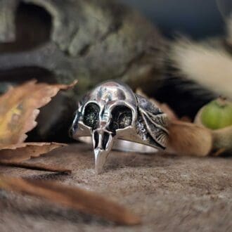 handcrafted sterling silver mens raven skull ring displayed on stone with soft focus bronze Greek helmet and autumnal setting