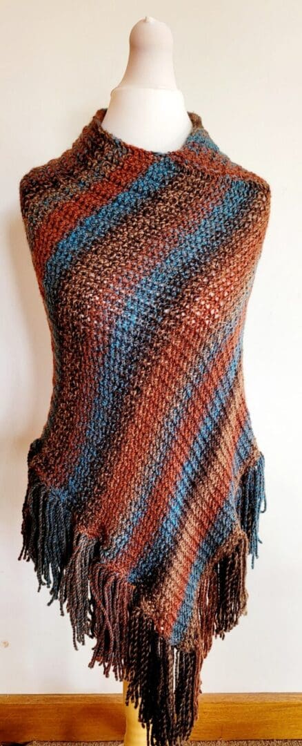 Brown and blue striped poncho with long tassels, shown from the front on a mannequin