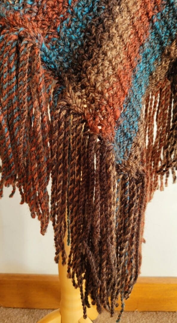 the end of a brown and blue knitted poncho showing the long brown and blue tassels