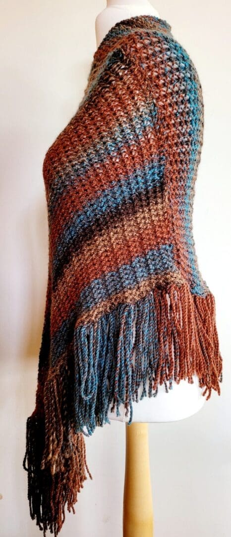 Brown and blue striped poncho with long tassels shown from the side on a mannequin