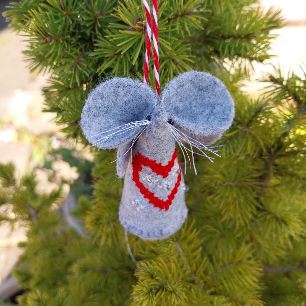 A hand stitched felt mouse with a red cross stitch heart design on the front