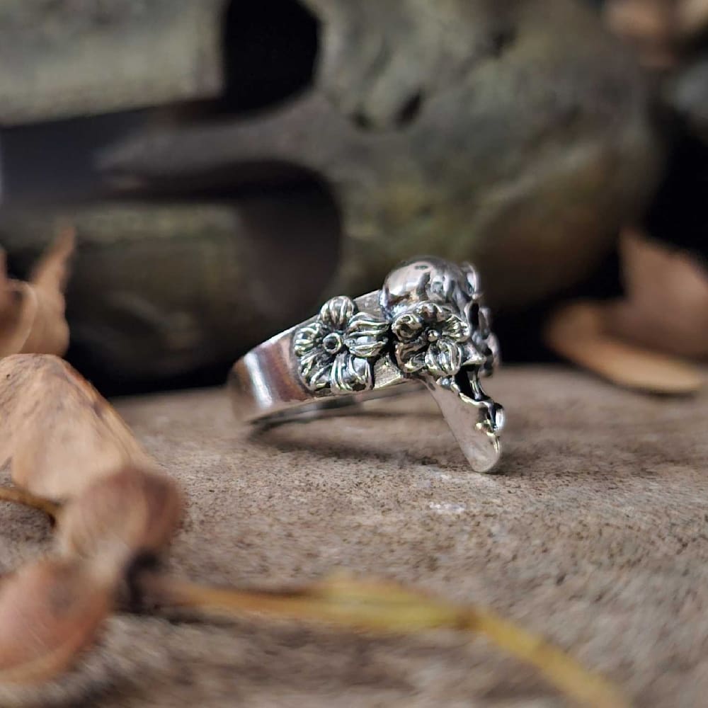 handcrafted sterling silver womens floral bird skull ring displayed on stone with soft focus bronze helmet and autumn setting