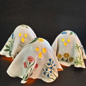 Three pottery ceramic ghosts decorated with William Morris floral design glow against a dark background.