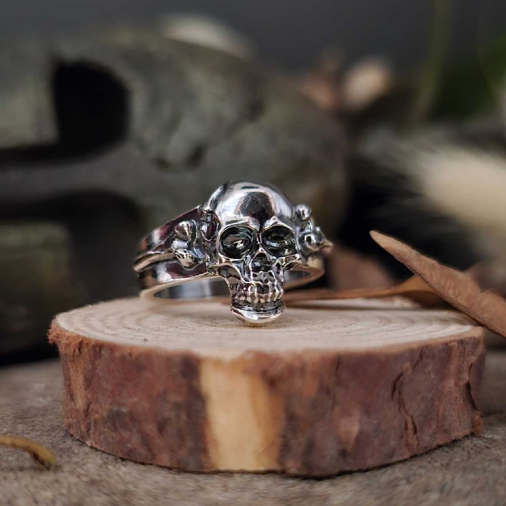 handcrafted sterling silver mens skull and bones ring displayed on wooden disk with soft focus ancient Greek helmet backing