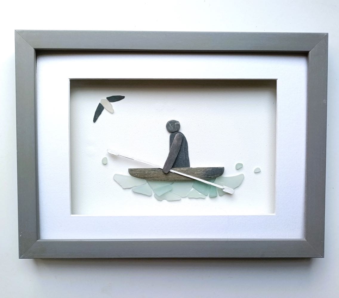 a framed picture of kayaker on a sea glass ocean made from stone and sea glass