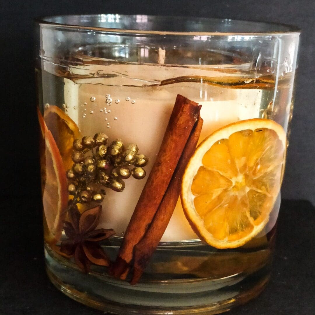 Large festive orange and spices botanical candle with real orange slices, cinnamon and star anise encapsulated in a clear gel wax with a central scented soy wax candle. The statement candle is shown against a dark background.