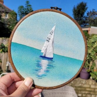 Hand embroidered sailing boat on a watercolour background hanging 6 inch hoop