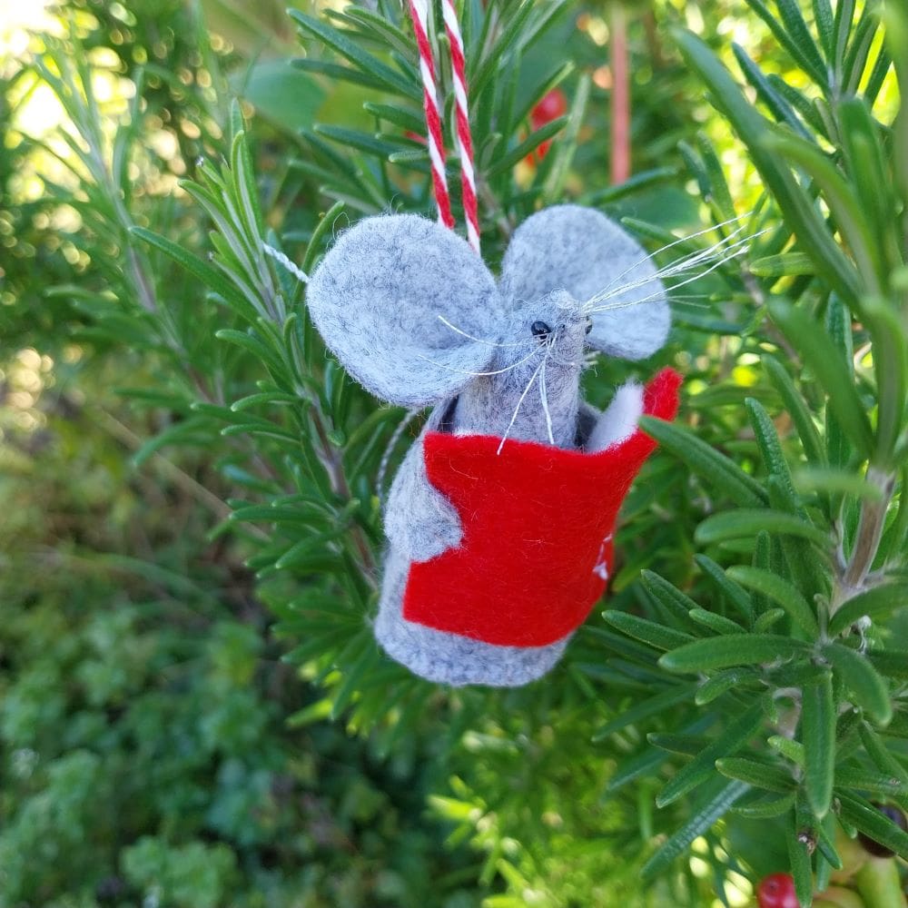 A hand stitched felt mouse holding a book of carols