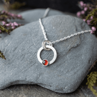 textured silver open circle pendant with small garnet stone set at the bottom. hung from silver chain