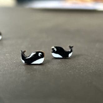 black and white handpainted wooden orca earrings on a dark background