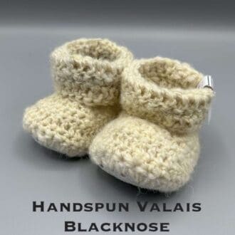 Pair of ecru baby booties crocheted with a sheepskin sole in handspun Valais Blacknose and Ryeland wool by Midge Porter Design