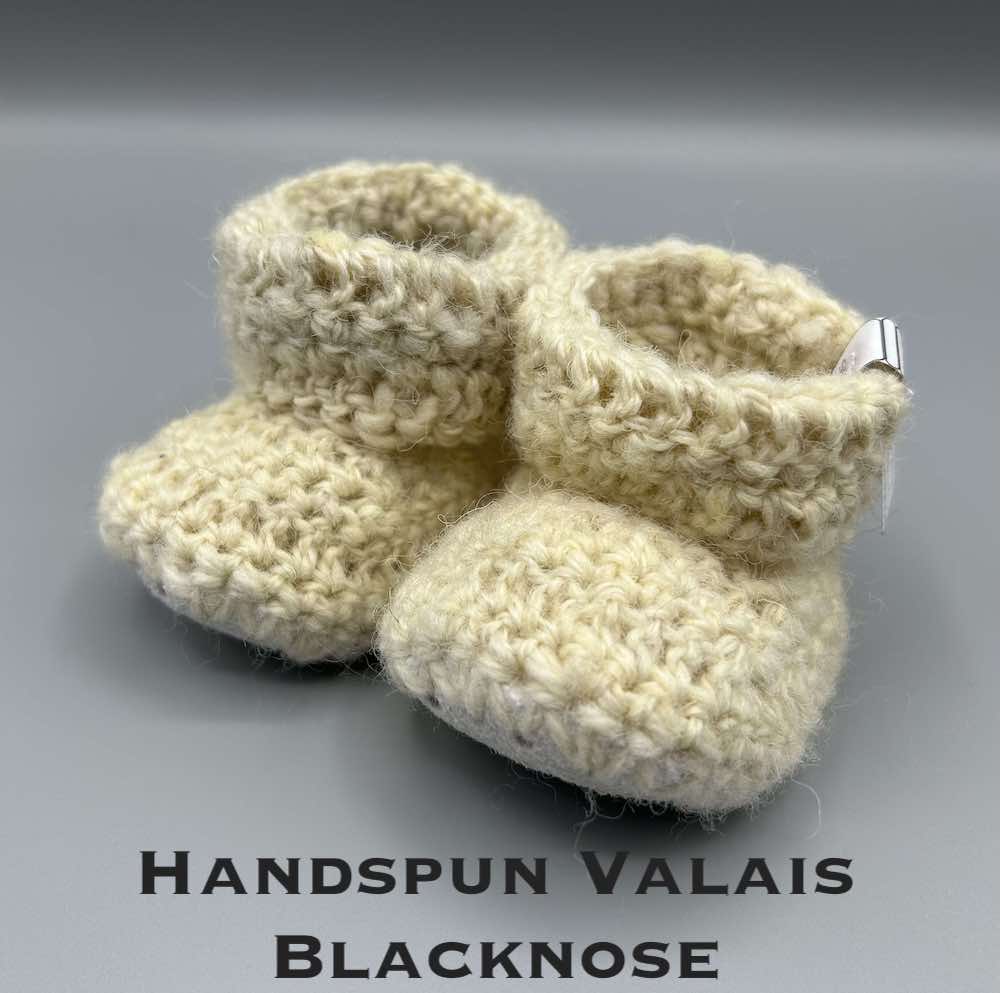 Pair of ecru baby booties crocheted with a sheepskin sole in handspun Valais Blacknose and Ryeland wool by Midge Porter Design