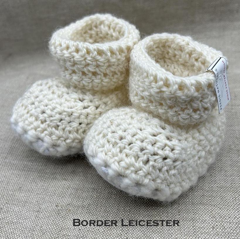 Pair of ecru baby booties crocheted with a sheepskin sole in Border Leicester wool by Midge Porter Design