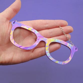 Quirky necklace for nerds. Shaped like a pair of spectacles. Faux leather and purple painted wood in a purple, pink, blue and yellow abstract painterly fabric design