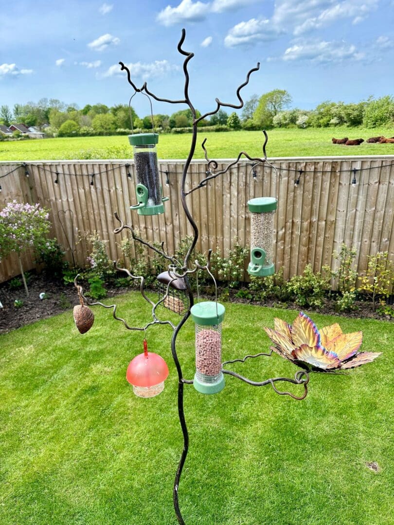 Beech leaf colourful stainless steel flower bird seed feeder and bird bath. Contemporary, robust and unusual bird feeder, handmade in the UK. Beautiful colours of golds, coppers , pinks and purples. On standard bird feeder tree bird feeding stand.