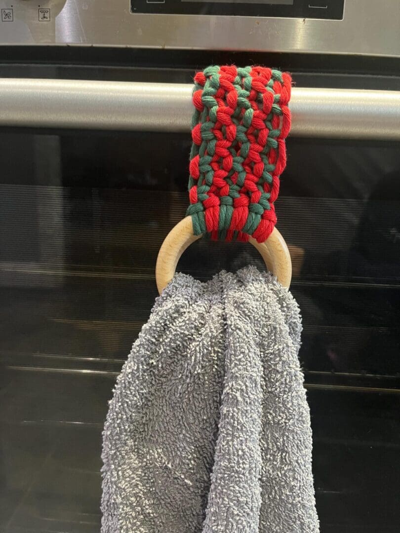 Handmade macrame tea towel holder, in festive Christmas colours of red and green, made with recycled cotton