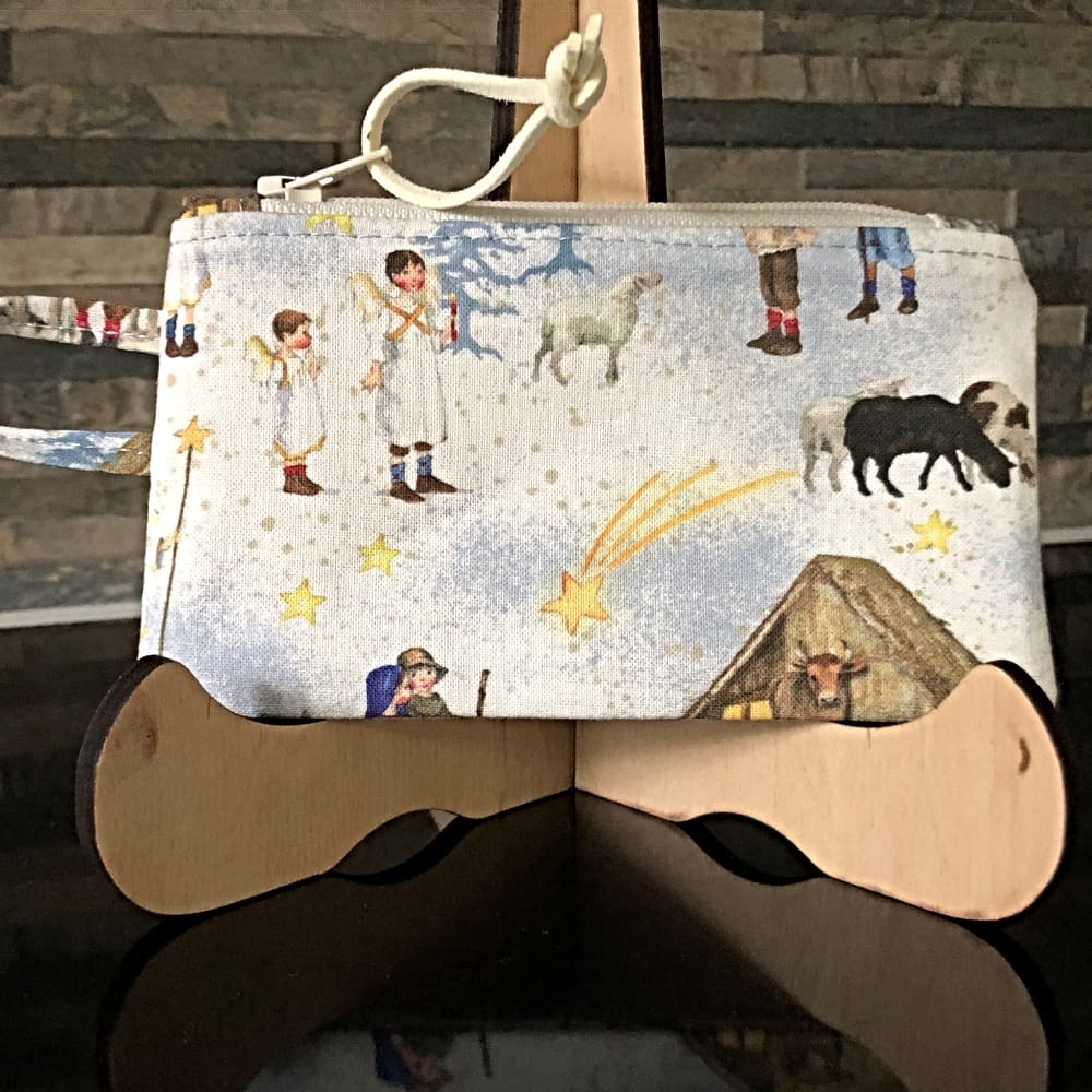 A coin purse in a nativity themed fabric with grey-blue tiny polka-dot lining. It features an integrated handle, perfect for attaching to keys or a lanyard..