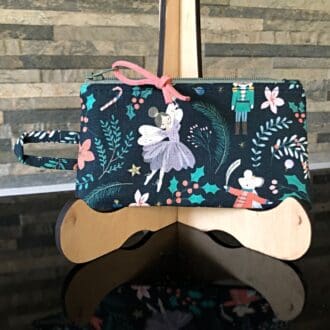 A blue purse designed for coins and cards, adorned with Nutcracker ballet figures and equipped with a built-in handle to attach to keys or a lanyard.