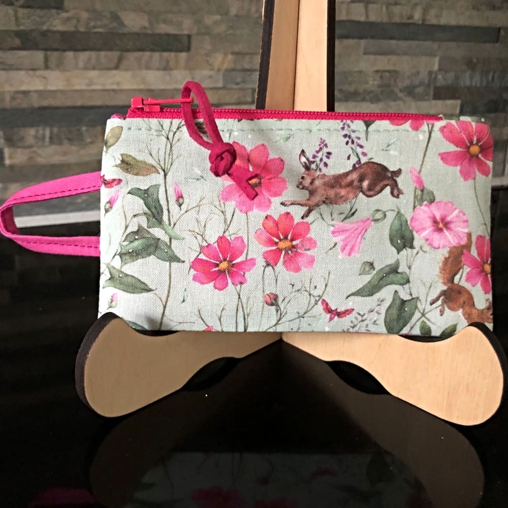 A pink and green purse designed for coins and cards, in a fabric reminiscent of summer. It features an integrated handle, perfect for attaching to keys or a lanyard..