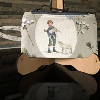 A coin purse in a winter themed fabric with a young boy shepherd highlighted, and a grey lining. It features an integrated handle, perfect for attaching to keys or a lanyard..