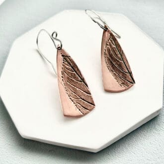 Copper drop earrings with a leal impressions and sterling silver ear wires.