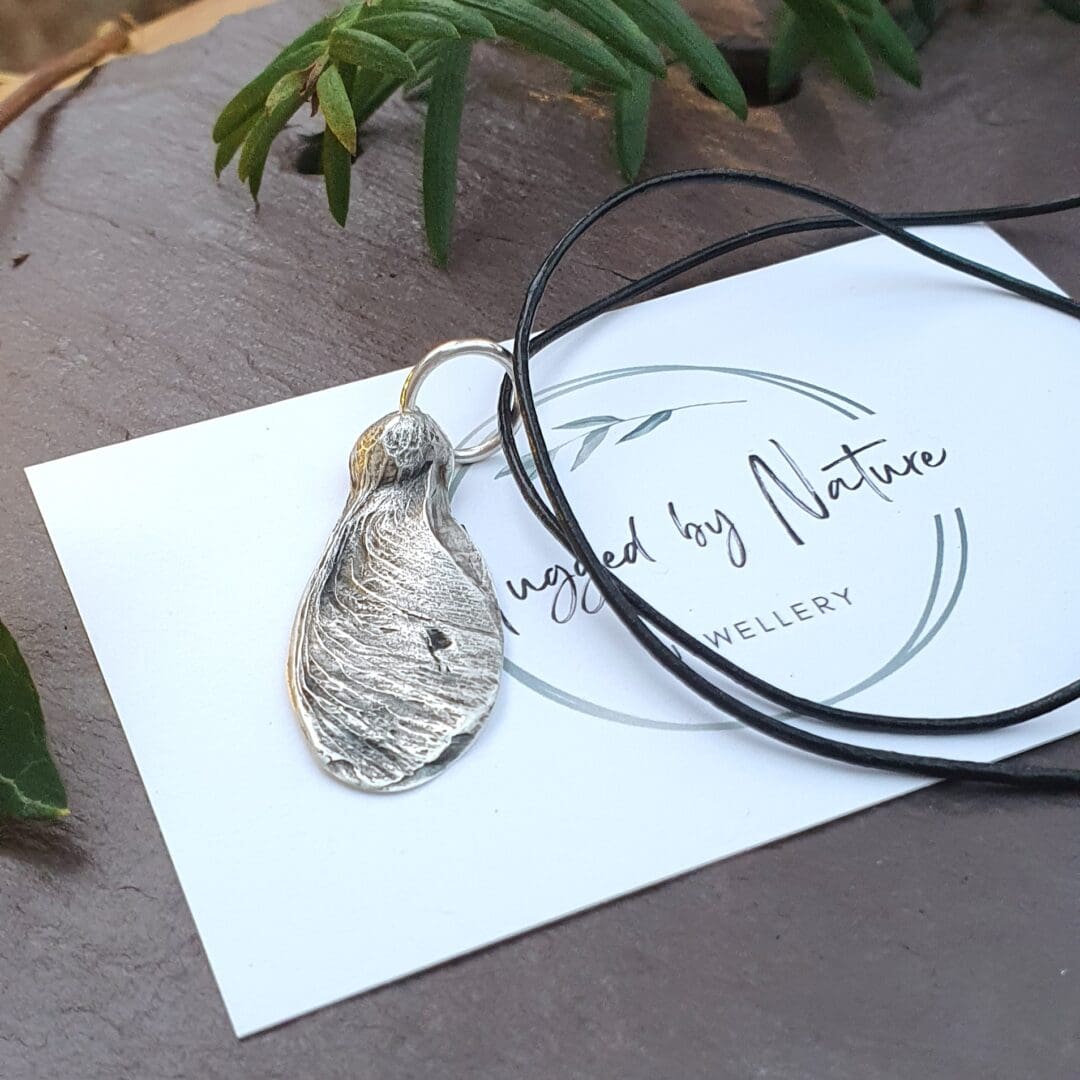 a solid silver sycamore seed on a leather cord displayed on a hugged by nature business card