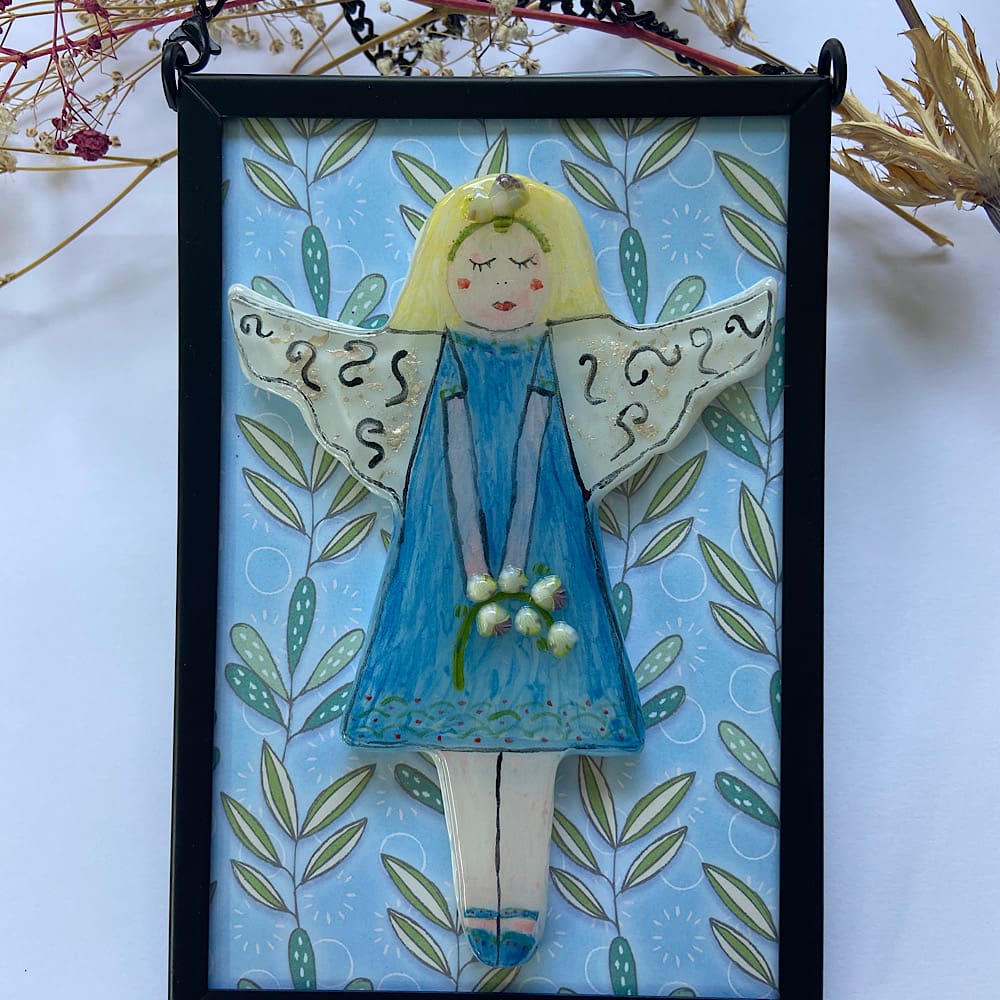 Fused glass fairy mounted on a black metal frame.