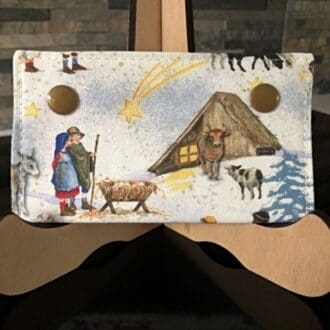 A softly padded fabric glasses case, featuring a nativity-themed design with a gold polka dot cotton interior, secured with gold Kam snaps.