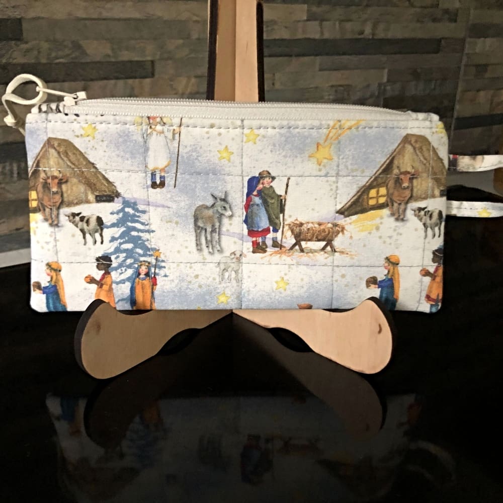 This is a compact, quilted phone wallet with nativity scenes against a cream and blue background. Finished with a cream zip, grey-blue tiny polka dot lining and faux suede zip pull.