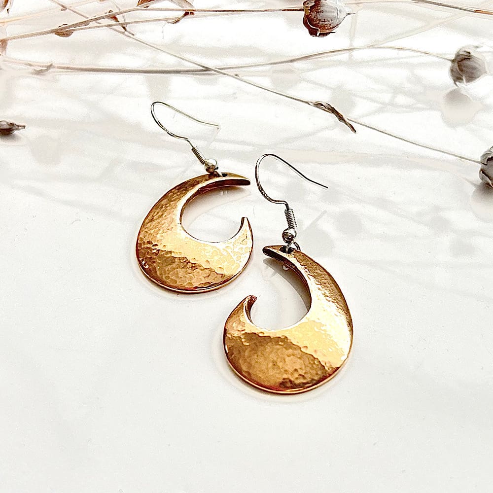 Bronze earrings in a half moon shape with sterling silver ear wires. Lay on a white surface.