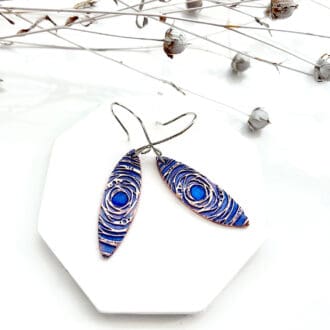 À pair of handmade copper earrings hand-painted with a blue metallic paint. They have sterling silver ear wires.