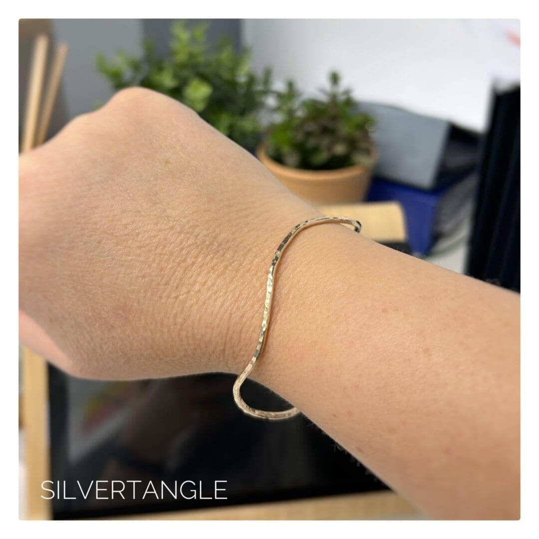 Wrist wearing a gold wavy hammered bangle