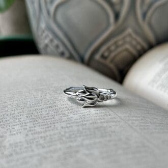 a delicate silver ring with a flower-style pattern on it lies on top of an open book. You can see a grey flower pot in the background.