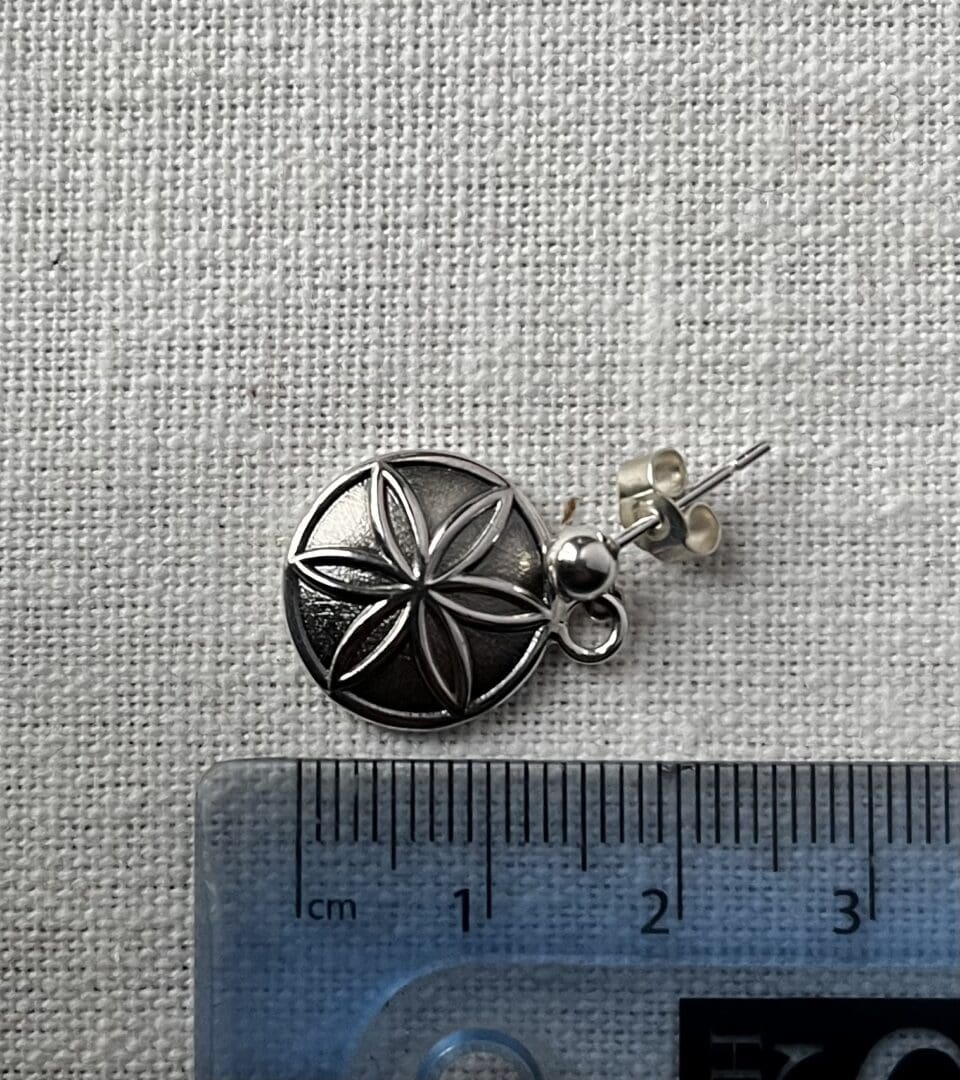 silver earring with hexafoil pattern is placed next to a ruler showing the total height which is 17mm