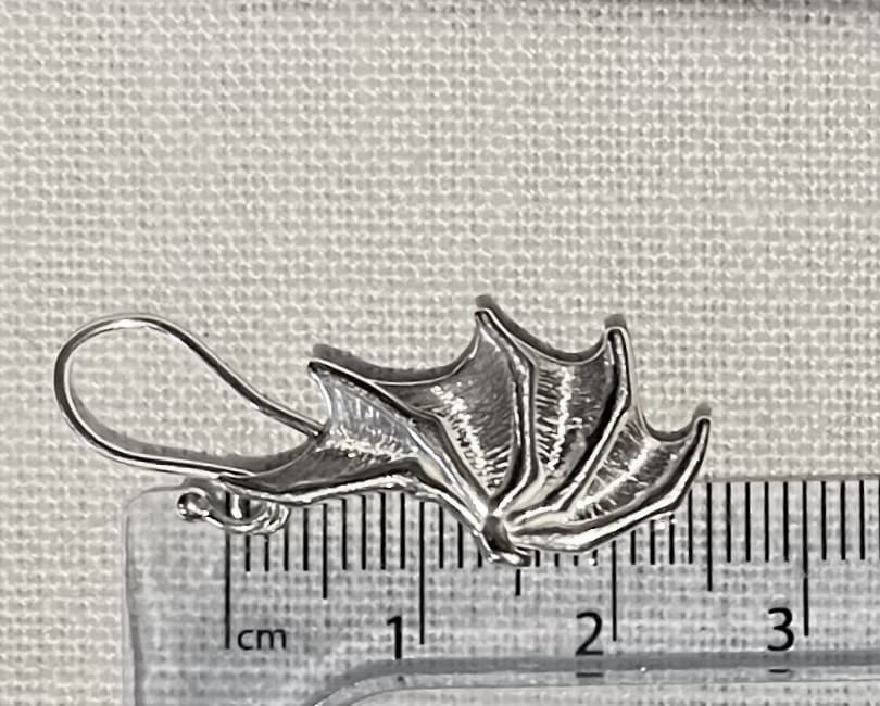 a silver earring in the shape of a dragon wing lies on top of a ruler showing the total height of the piece to be 25mm