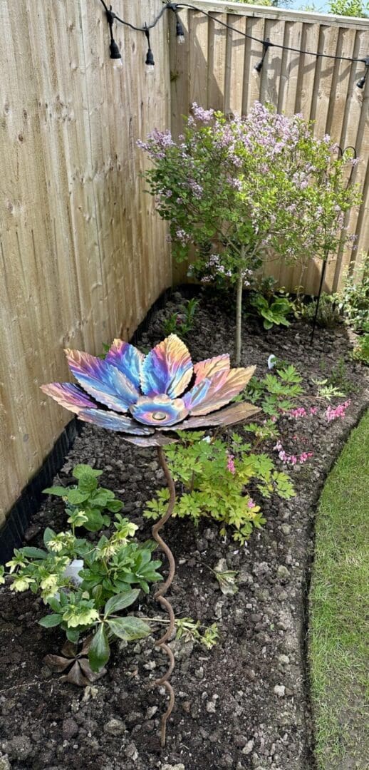 Beech leaf colourful stainless steel flower bird seed feeder and bird bath. Contemporary, robust and unusual bird feeder, handmade in the UK. Beautiful colours of golds, coppers , pinks and purples. On standard bird feeder tree bird feeding stand.