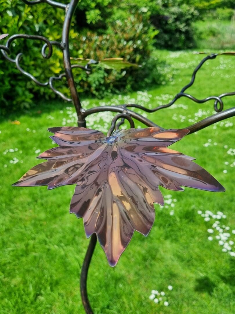 Detail of Maple leaf with vibrant autumn colours of golds, coppers, pink and purple, design craftmanship, stylish bird feeder tree stand.