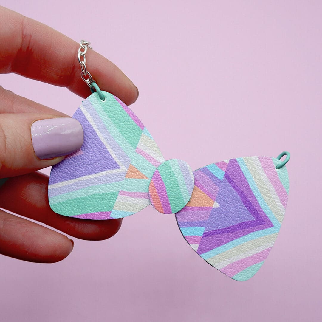 Pretty pastel Kawaii Core necklace in the shape of a bow tie. Held in white woman's hand at an angle