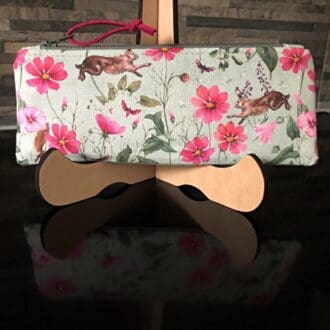 A pencil case featuring pink and green floral fabric with hares and red squirrels.