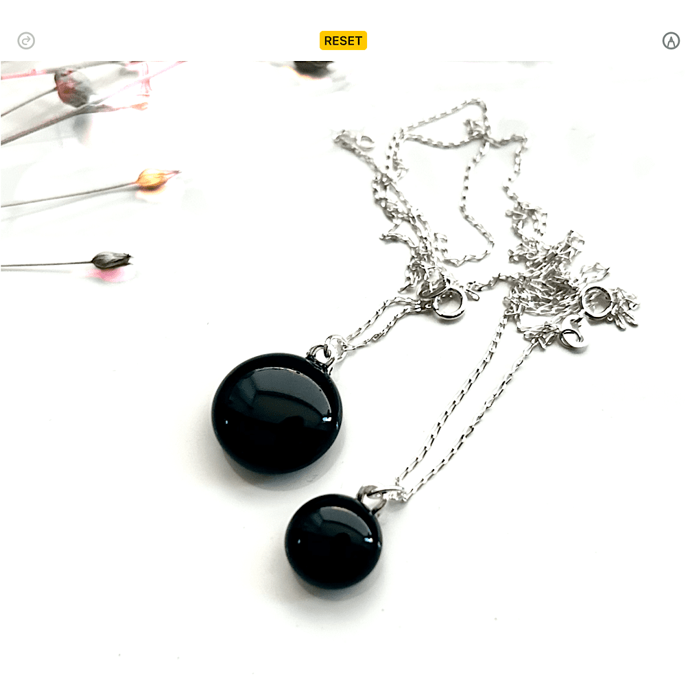 Two small black fused Glass cabochon pendants one largeur than the other, with a sterling silver chain. On a White background.