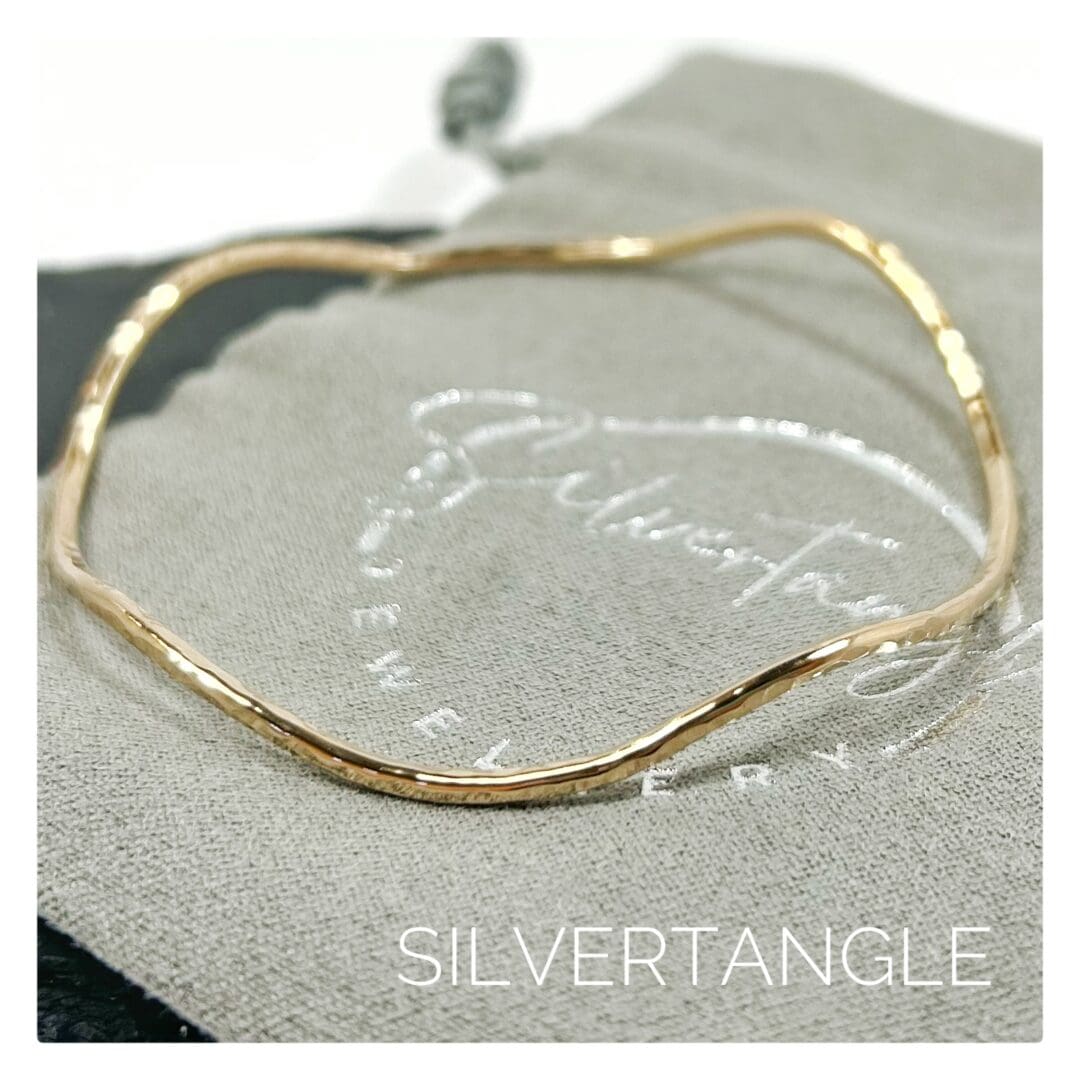 Wavy Gold Hammered Bangle sitting on a grey branded bag